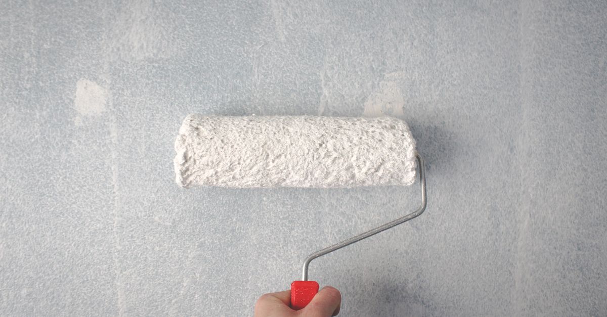 A person's hand using a paint roller to apply white paint on a wall.