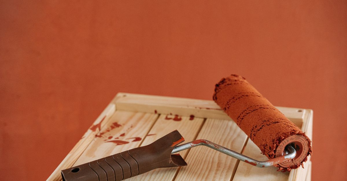 A paint roller with rustic brown paint on a wooden surface against an earthy wall.