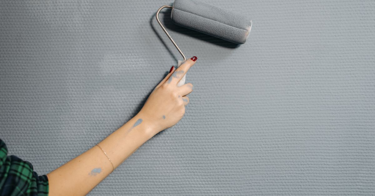 A close-up of a person's hand using a paint roller on a blue wall for home renovation.