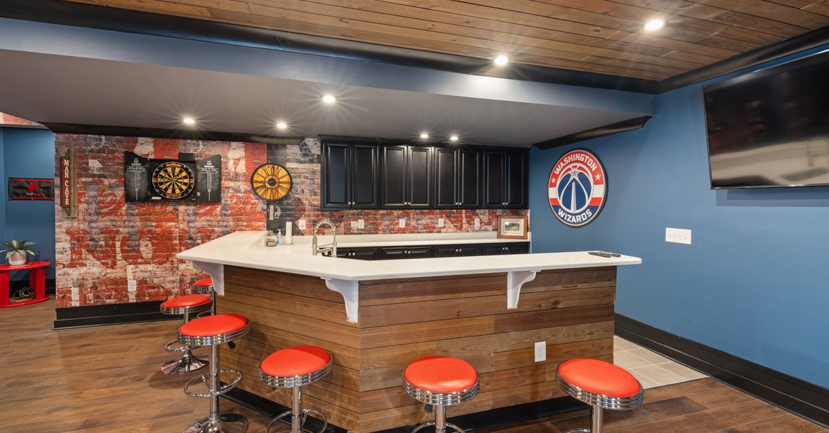Stylish home bar with vibrant decor, featuring a Washington Wizards theme, dart board, and red bar stools.