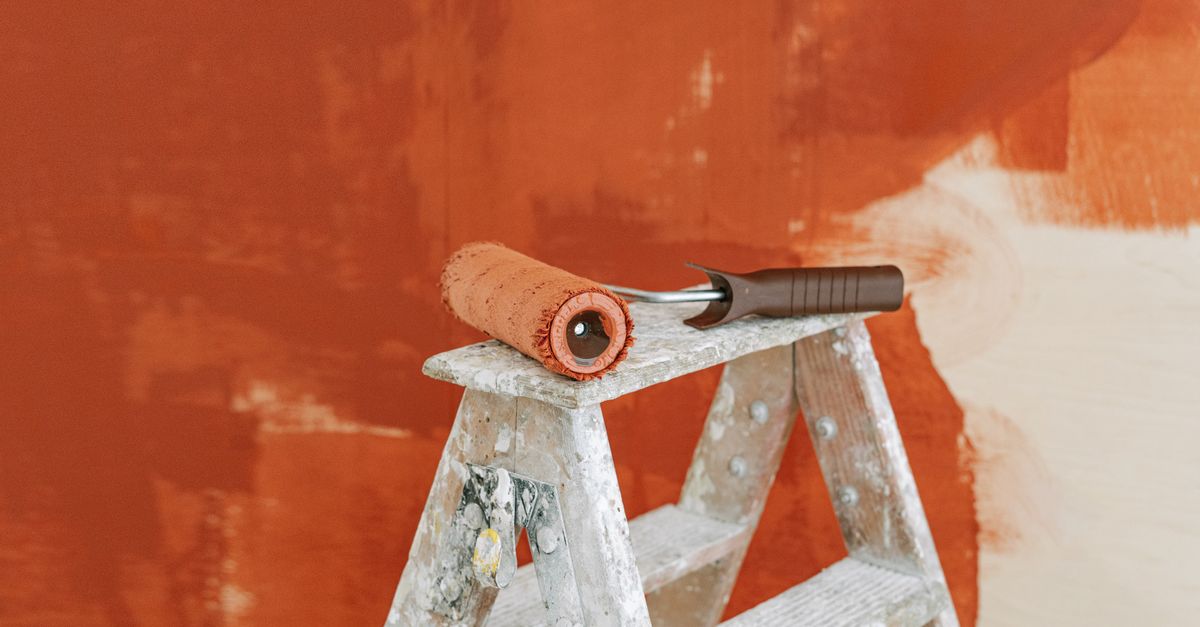 Paint roller on a ladder with a partially painted red wall in the background.
