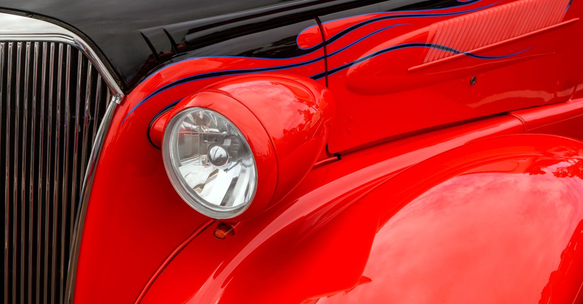 Close-up of a vintage car's vibrant red hood with custom flame detailing.