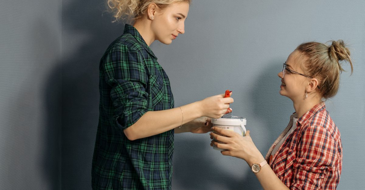 Two women working together on a home renovation, mixing paint indoors.