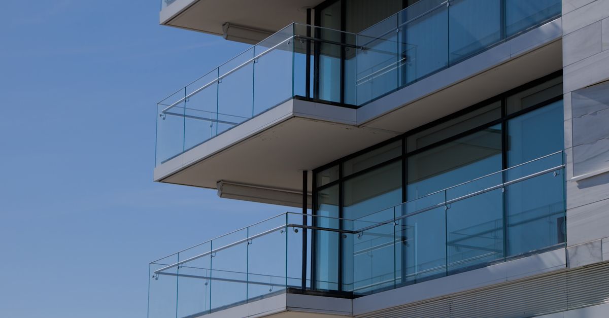 Sleek modern building with glass balconies against a clear blue sky, showcasing architectural design.