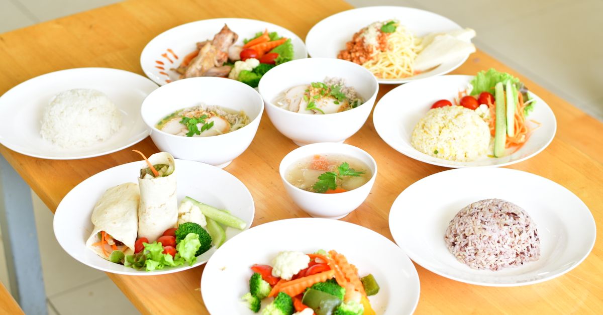 A variety of healthy dishes including rice, soup, and vegetables served on a wooden table.