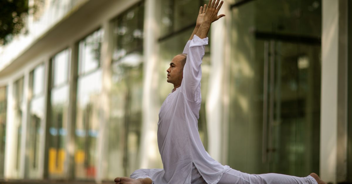 Side profile of a man performing yoga outdoors, stretching in a white outfit, showcasing relaxation and mindfulness.