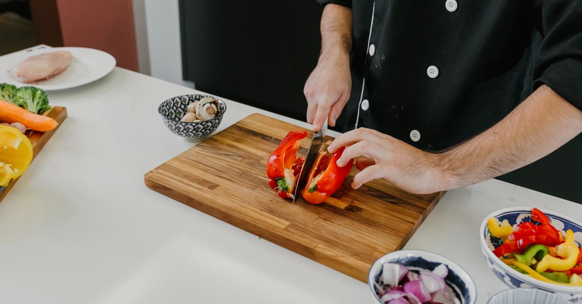 Chef slicing fresh bell peppers on a wooden board in a modern kitchen.