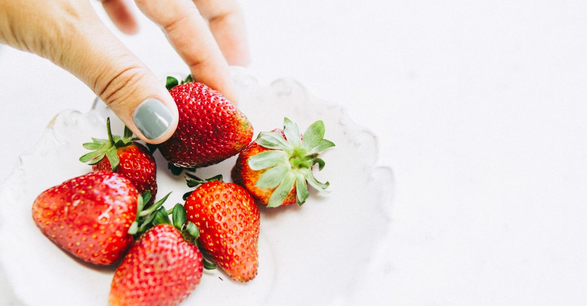 Bright and fresh strawberries being held over a white ceramic bowl, evoking a healthy lifestyle.