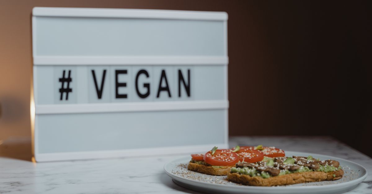 Delicious vegan avocado toast with tomatoes on marble table beside vegan sign.