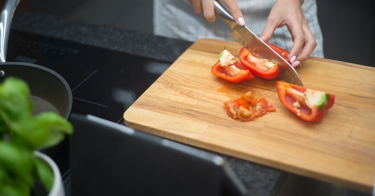 Close-up of a woman slicing red bell pepper in a modern kitchen setting.