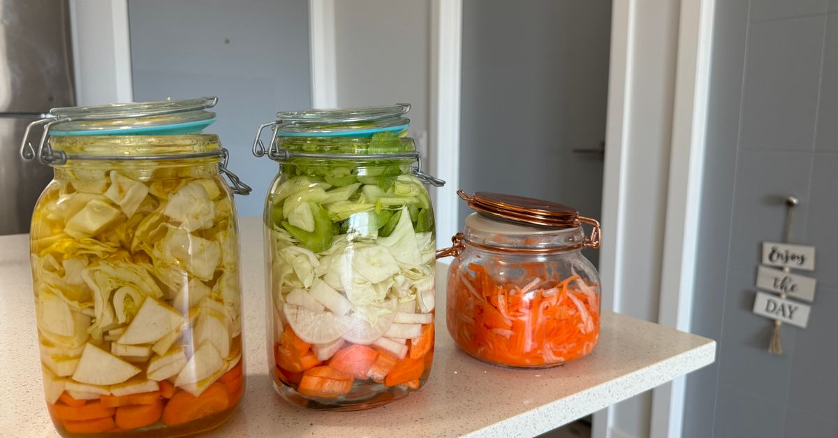 Three jars filled with colorful homemade pickled vegetables on a kitchen counter.