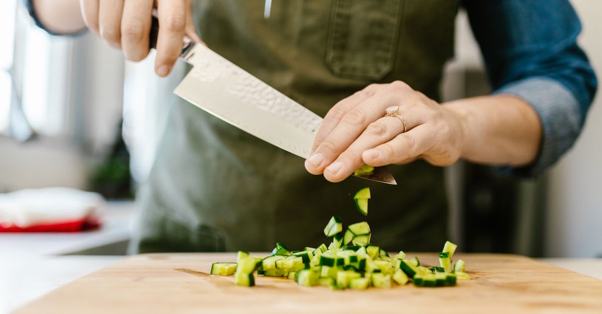 Close-up of a chef slicing cucumbers on a wooden board with precision.