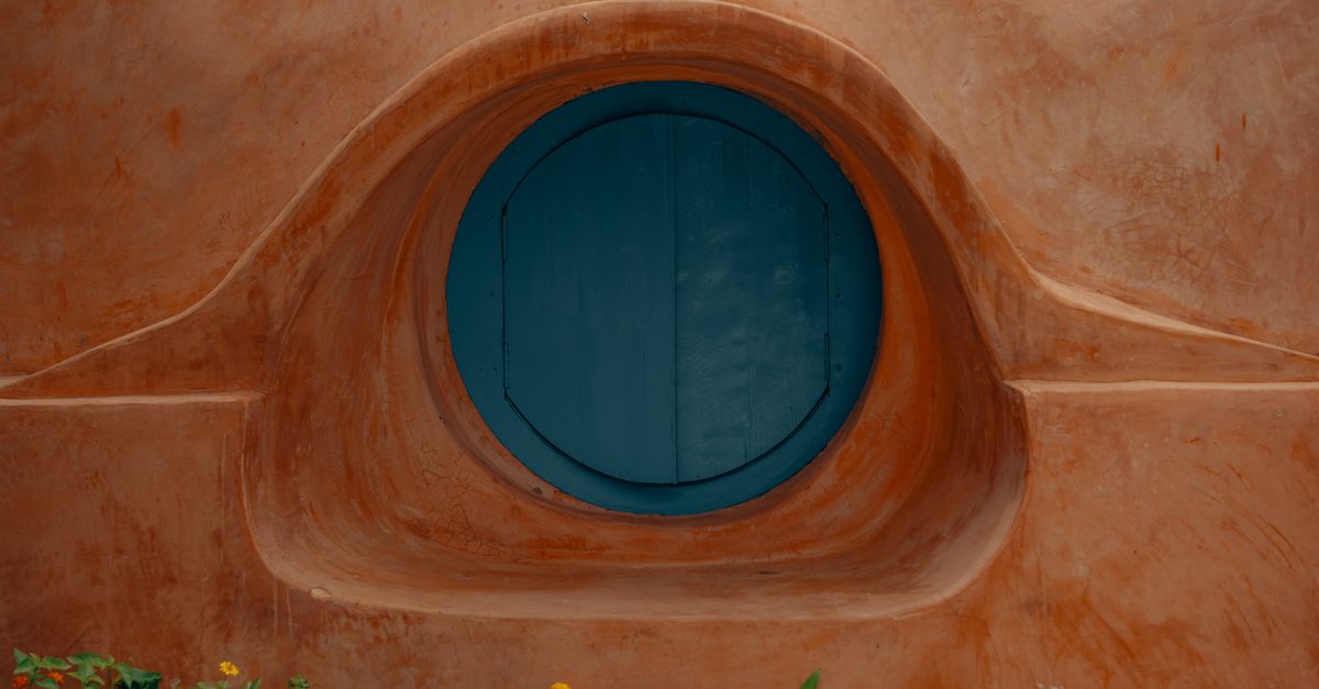 Close-up of a round blue window set in a rustic terracotta wall in Hyderabad, India.