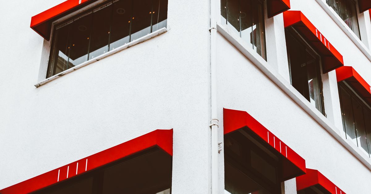 Angular view of a building featuring bold red awnings and large windows.