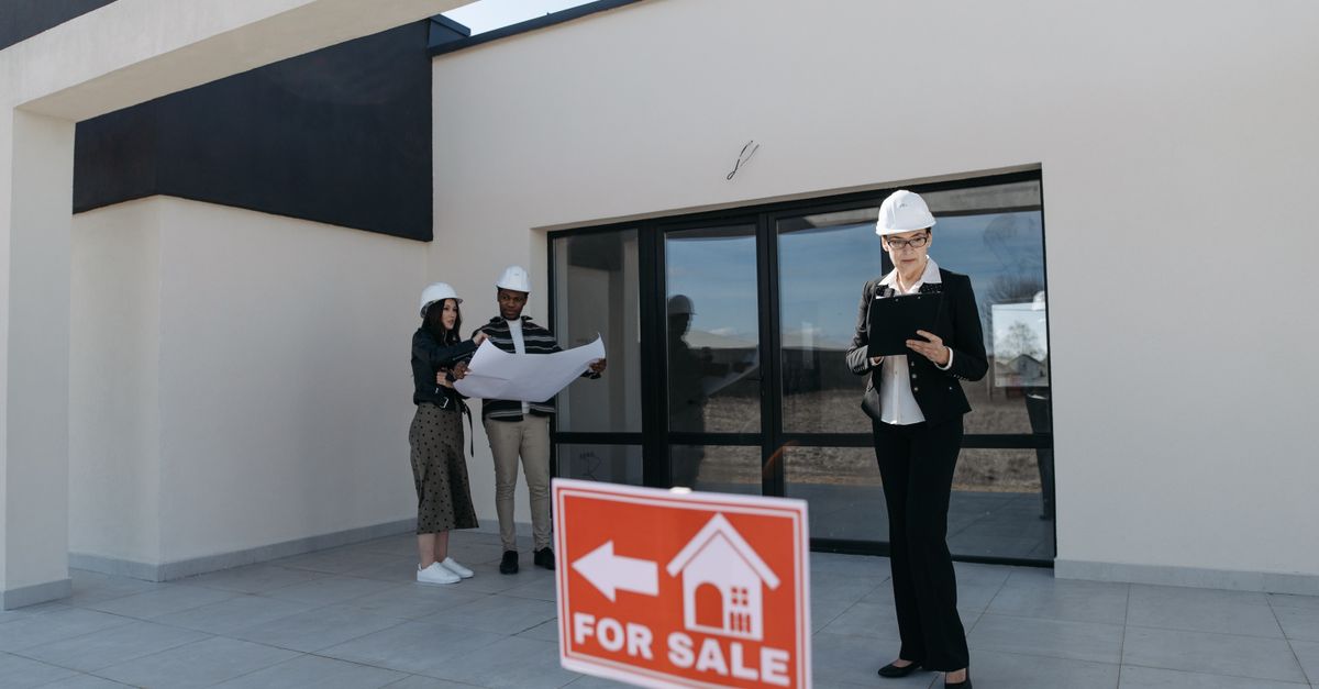Real estate agents in hard hats reviewing plans beside a house for sale.