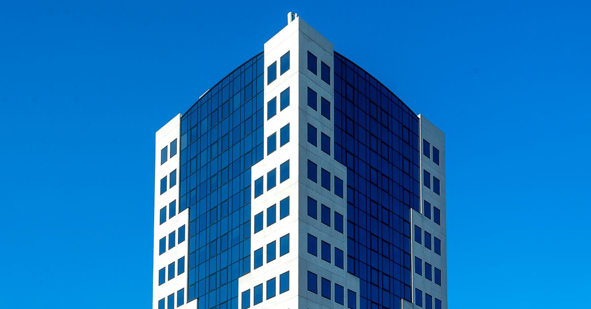 Modern high-rise office building with reflective windows set against a clear blue sky.