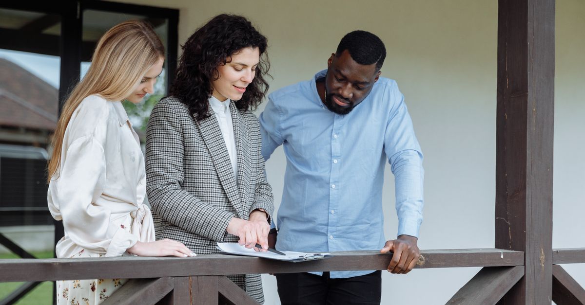 Real estate agent discussing property paperwork with a couple on a porch.
