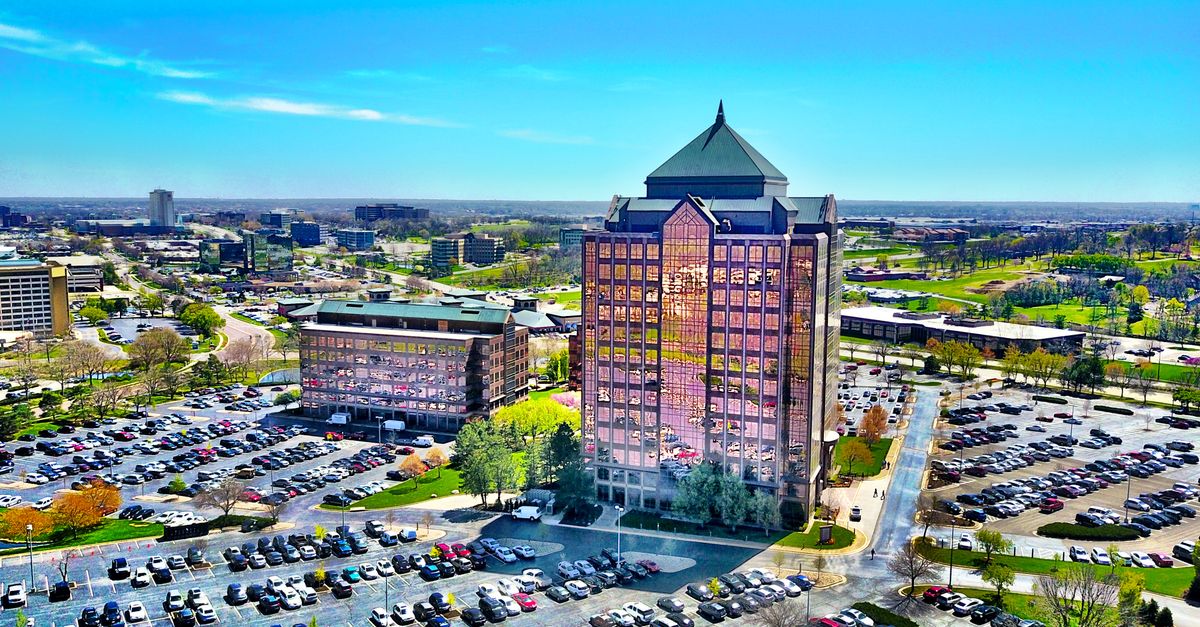Bird's-eye view of a modern skyscraper and parking lot in Overland Park, KS, under a clear blue sky.