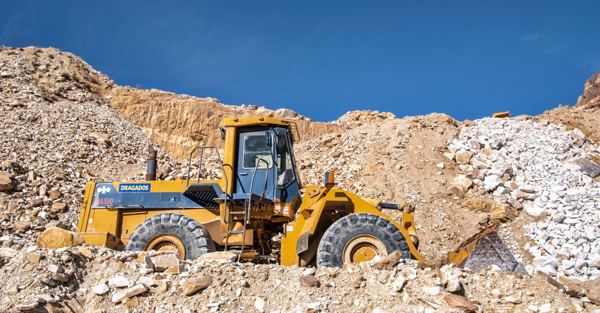 Industrial bulldozer operating in a sunny quarry with rocky terrain.