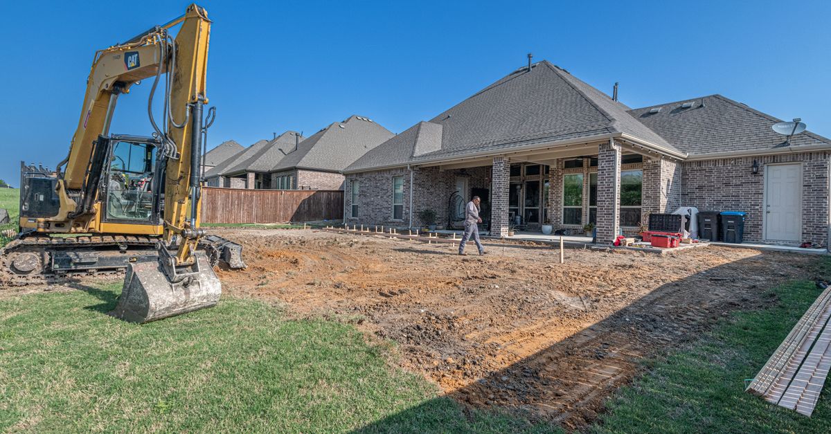 A construction site for a new patio in a Texas backyard with heavy machinery.