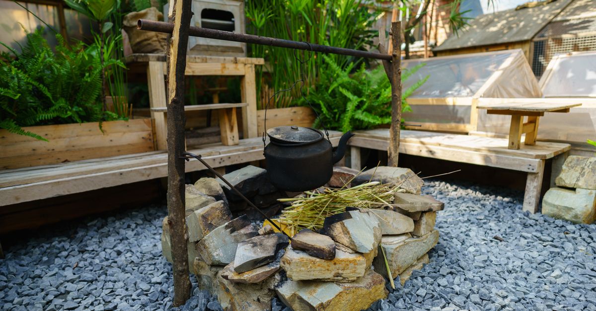 Cozy outdoor cooking area with a stone firepit and vintage pot, set in a lush garden environment.