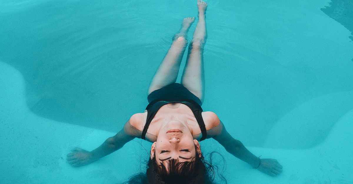 A woman in a black swimsuit floats gracefully in a serene swimming pool.
