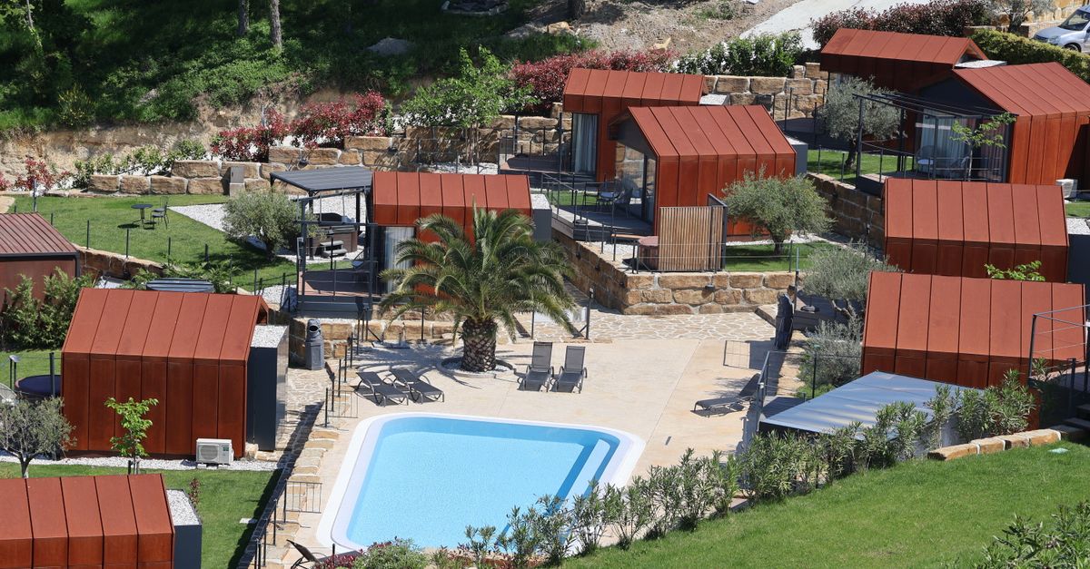 Aerial view of a modern resort featuring red roof cabins and a central swimming pool.