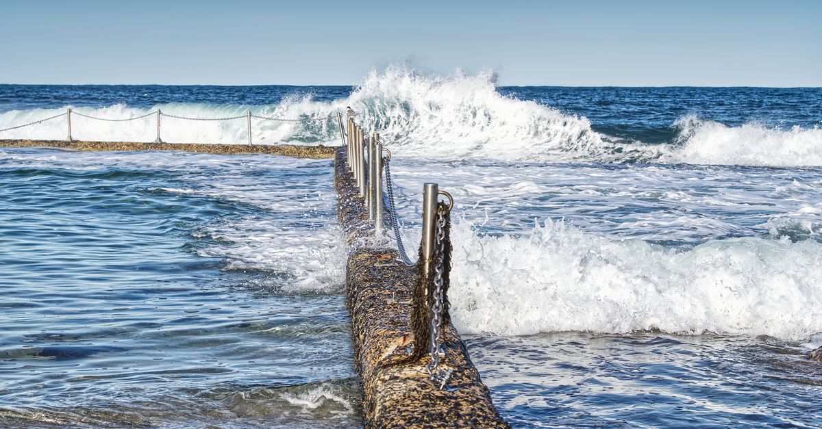 Dramatic ocean scene with waves crashing over a swimming pool barrier. Perfect for coastal themes.