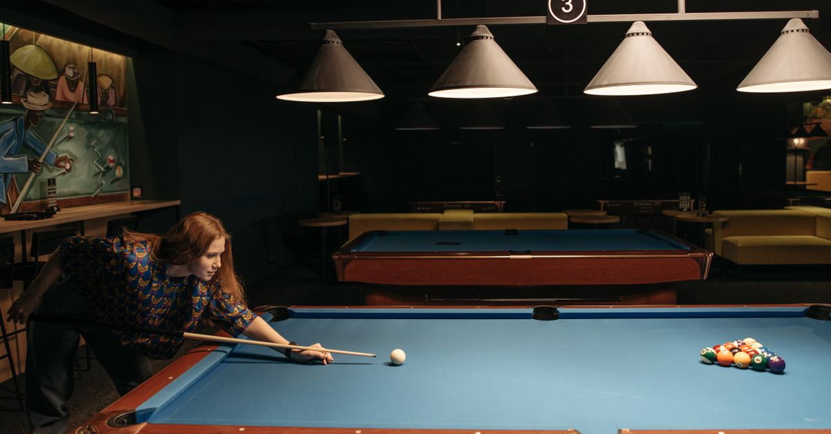 Woman enjoying a game of billiards in a dimly lit indoor setting, aiming at the balls.