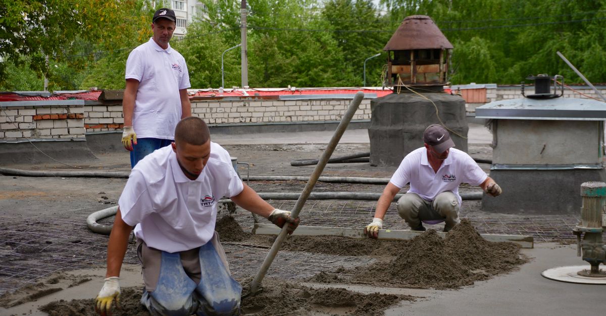 Three workers troweling and leveling cement on a rooftop construction project.