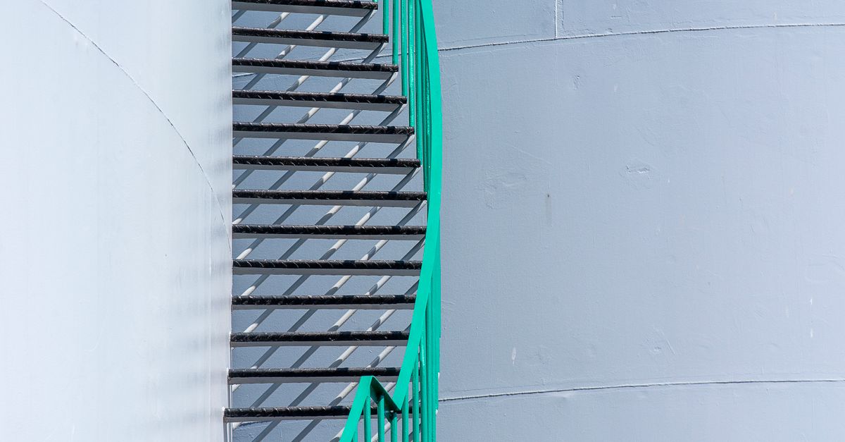 Close-up view of a green spiral staircase on a large industrial storage tank.