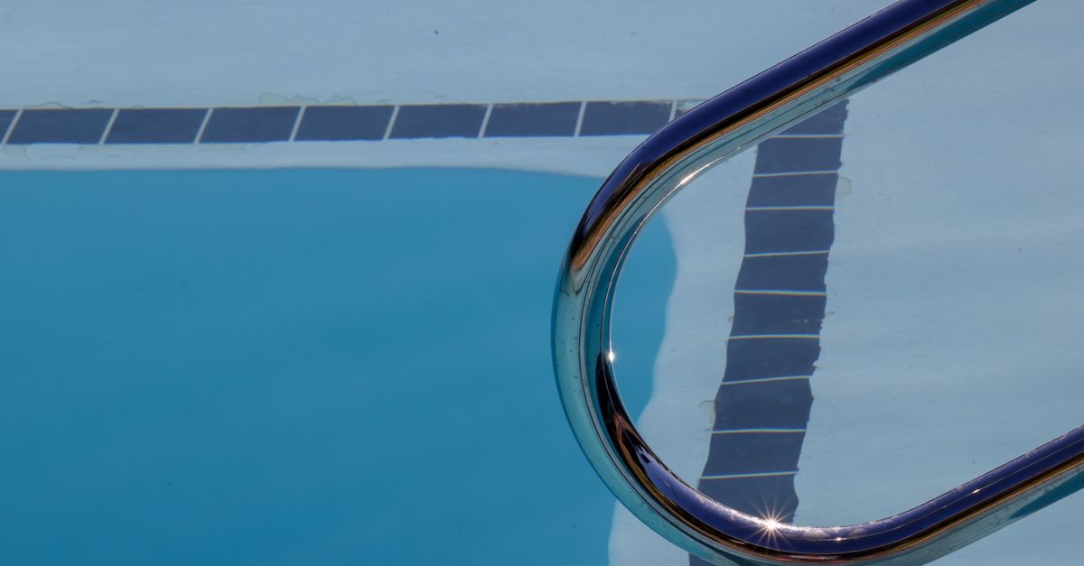 Dynamic view of a swimming pool with ladder reflecting sunlight on the water surface.