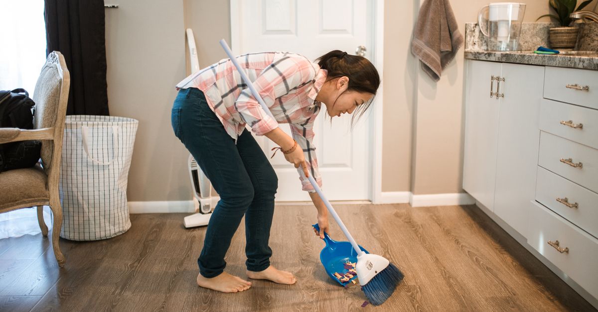 An Asian woman performing cleaning chores by sweeping the floor indoors.