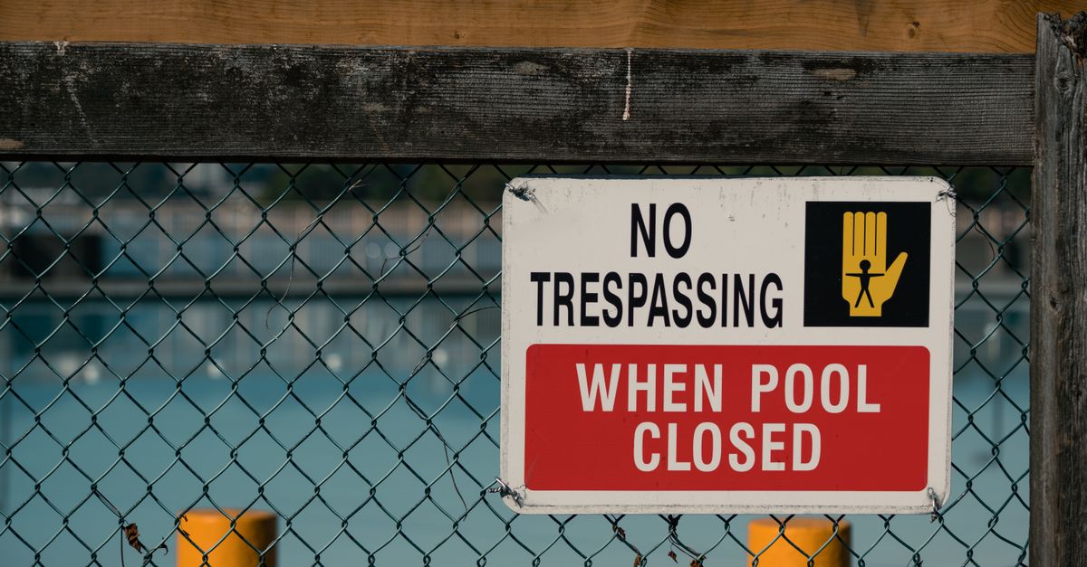 A 'No Trespassing' sign on a chain link fence at a closed swimming pool, ensuring safety and security.