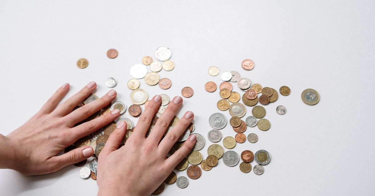 Hands arranging a variety of international coins on a neutral light background.
