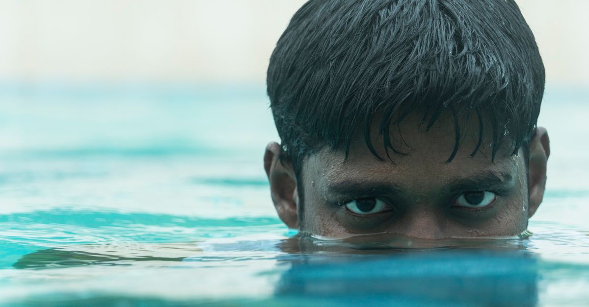 A man with intense eyes looks closely above the waterline in a swimming pool.