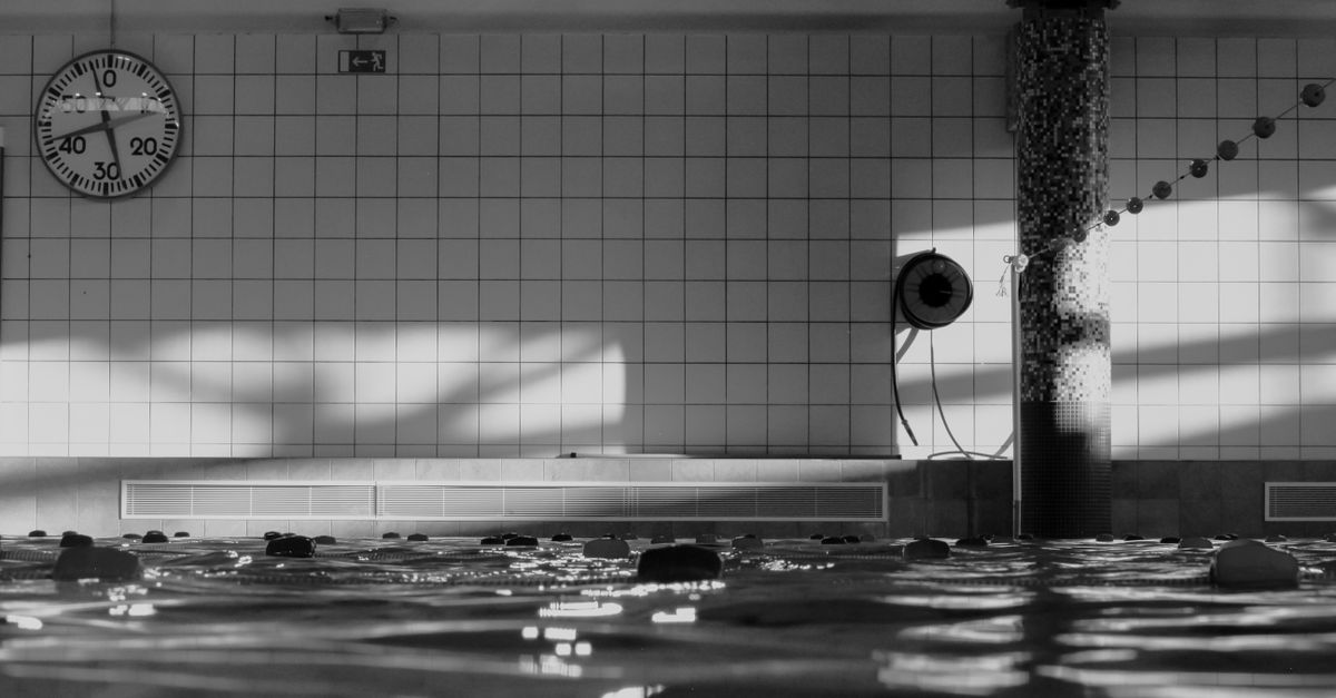 Monochrome view of indoor swimming pool with clock and tiles.