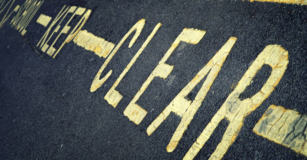 Close-up of yellow road markings with 'KEEP CLEAR' instruction on asphalt surface.