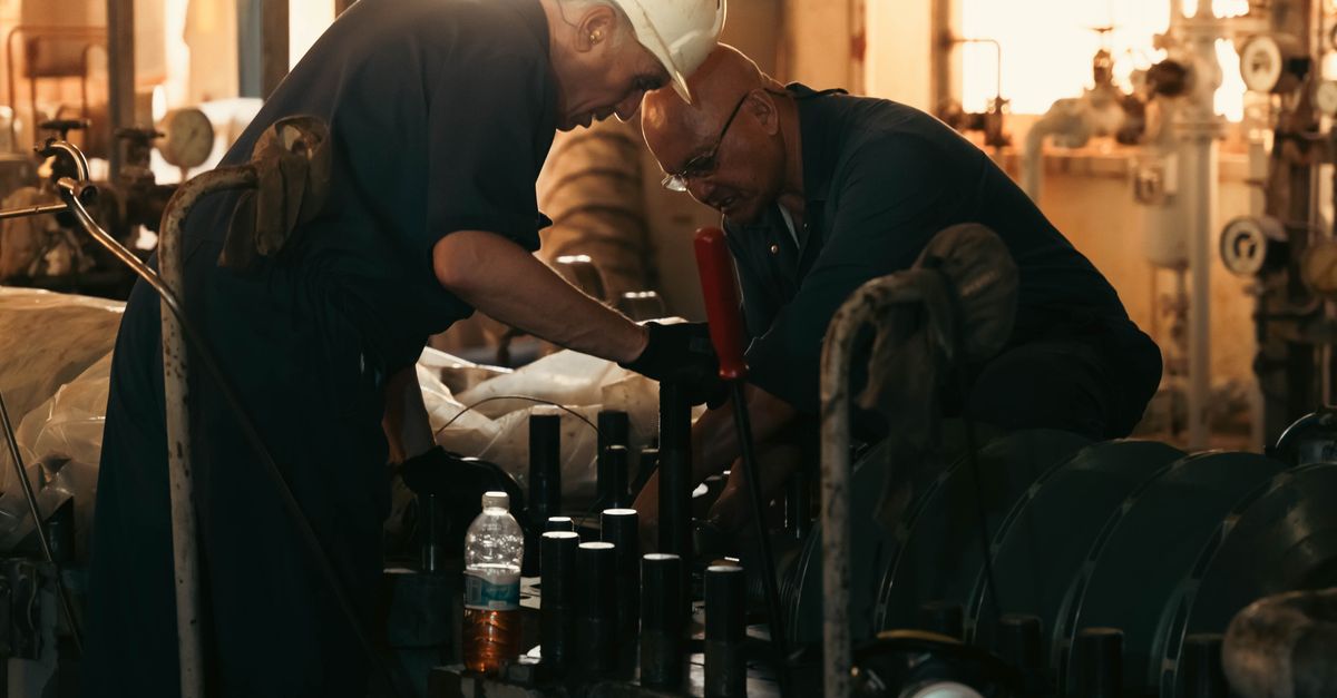Two engineers collaborating on machinery maintenance in a dimly lit industrial plant.