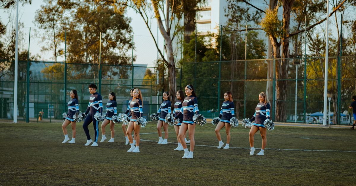 Cheerleading squad practicing routines on an outdoor field during sunset.