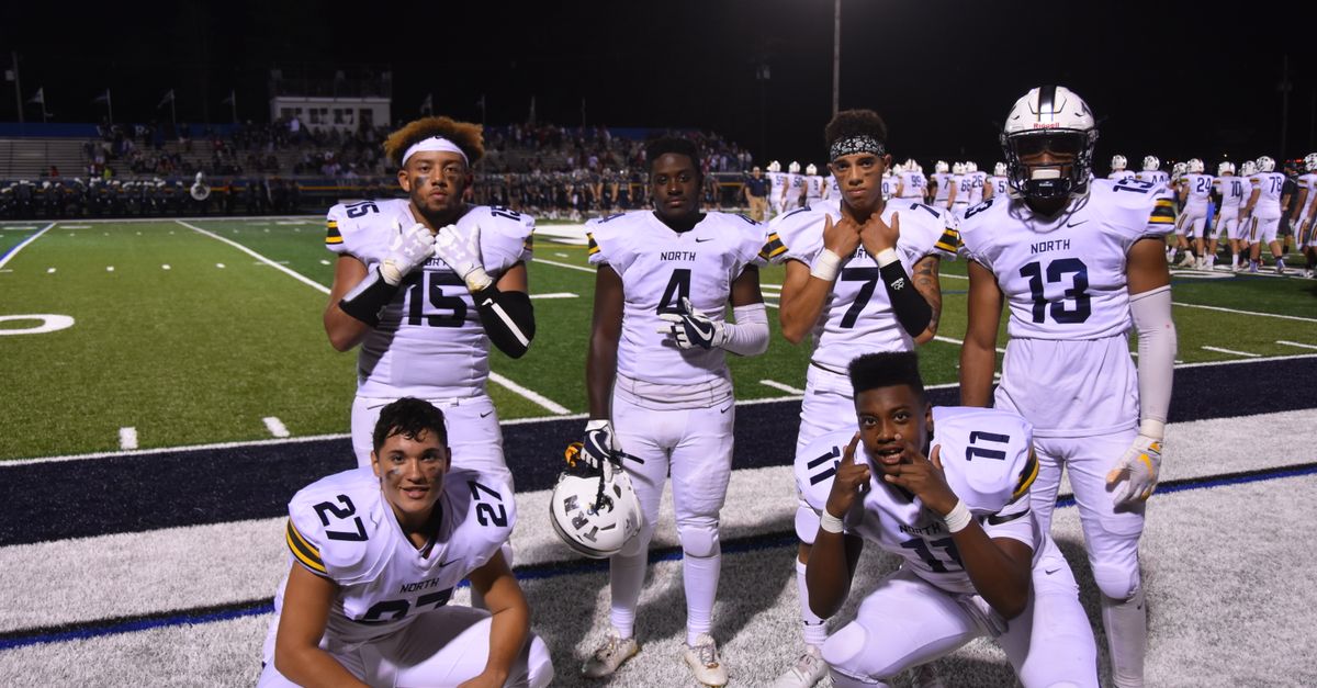 A group of high school football players posing on the field at night, wearing uniforms.