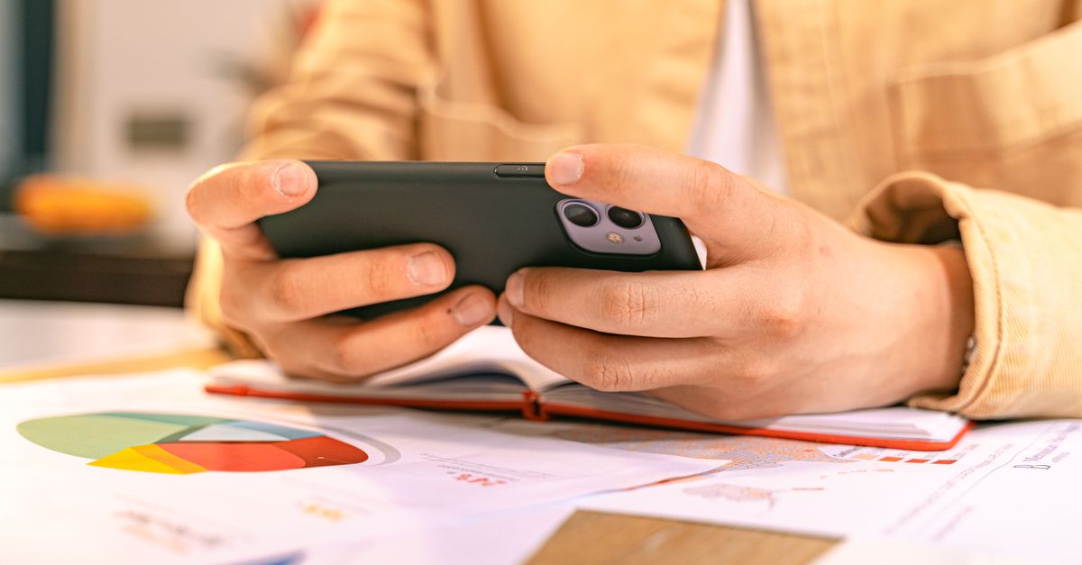 A business person checking their phone while working with graphs and charts on a desk.