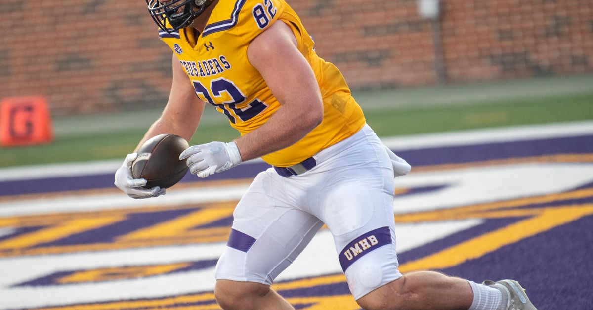 Athlete in yellow jersey scores a touchdown during a college football game outdoors.