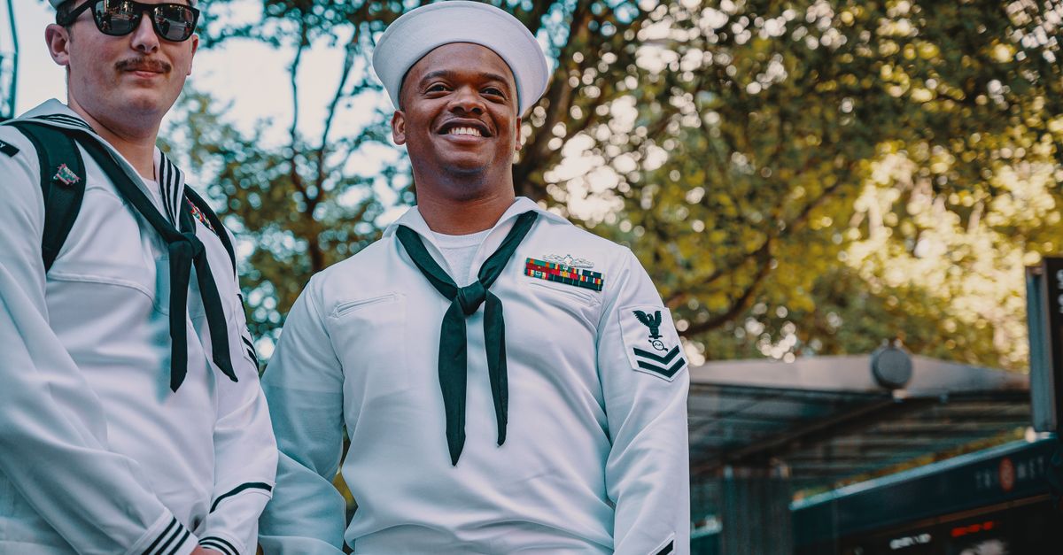 Two navy sailors in uniform smiling outdoors, capturing camaraderie and pride.