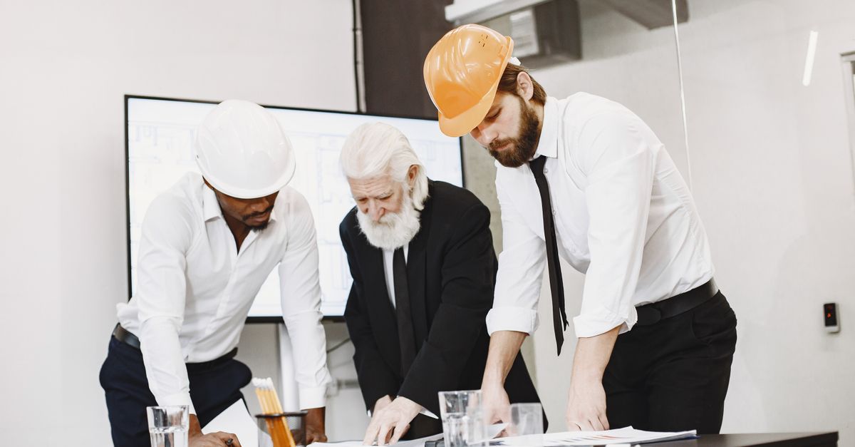Group of architects discussing construction blueprints wearing hardhats in a modern office.