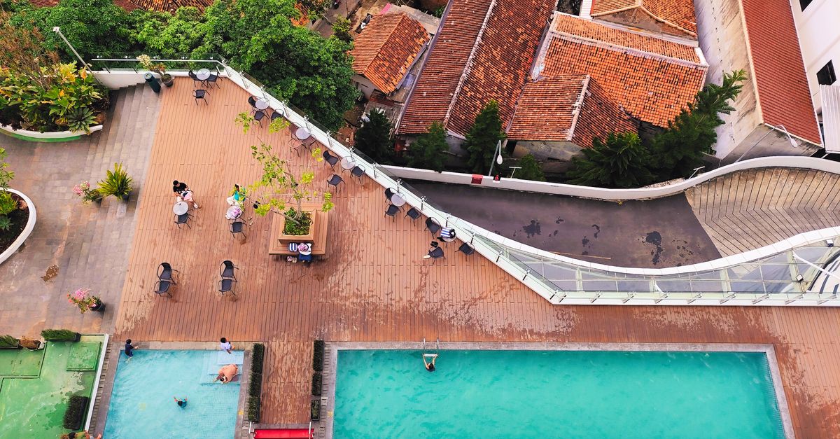 Aerial view of a rooftop pool area with swimmers and vibrant cityscape backdrop.