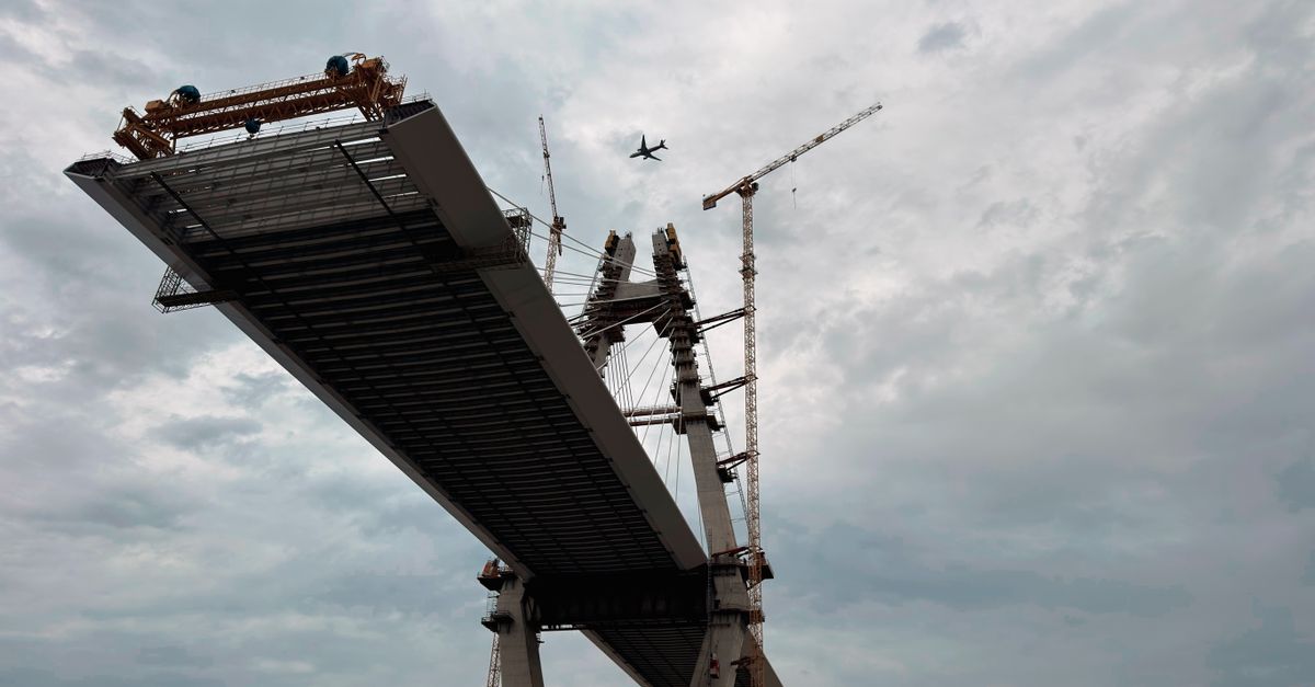 Dynamic shot of bridge construction site with a plane flying overhead.