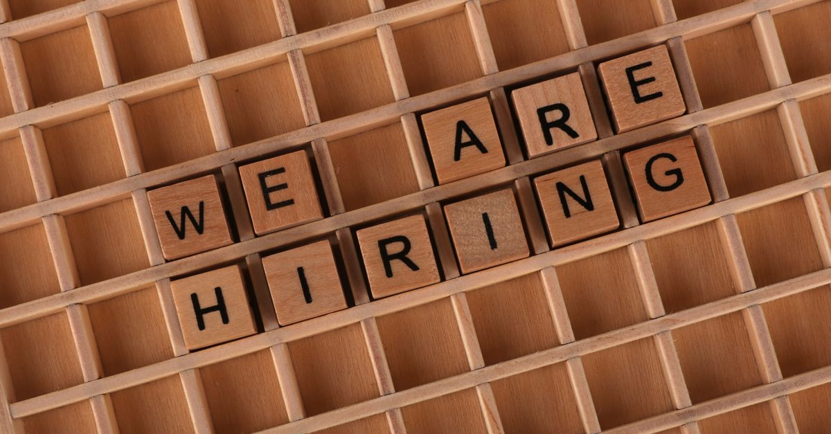 Wooden letter tiles arranged to spell 'We Are Hiring' on a wooden grid background.