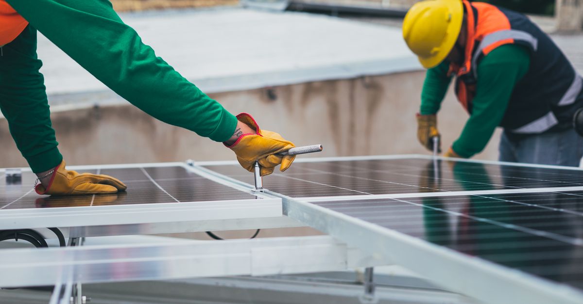 Workers secure solar panels on a rooftop, advancing renewable energy.