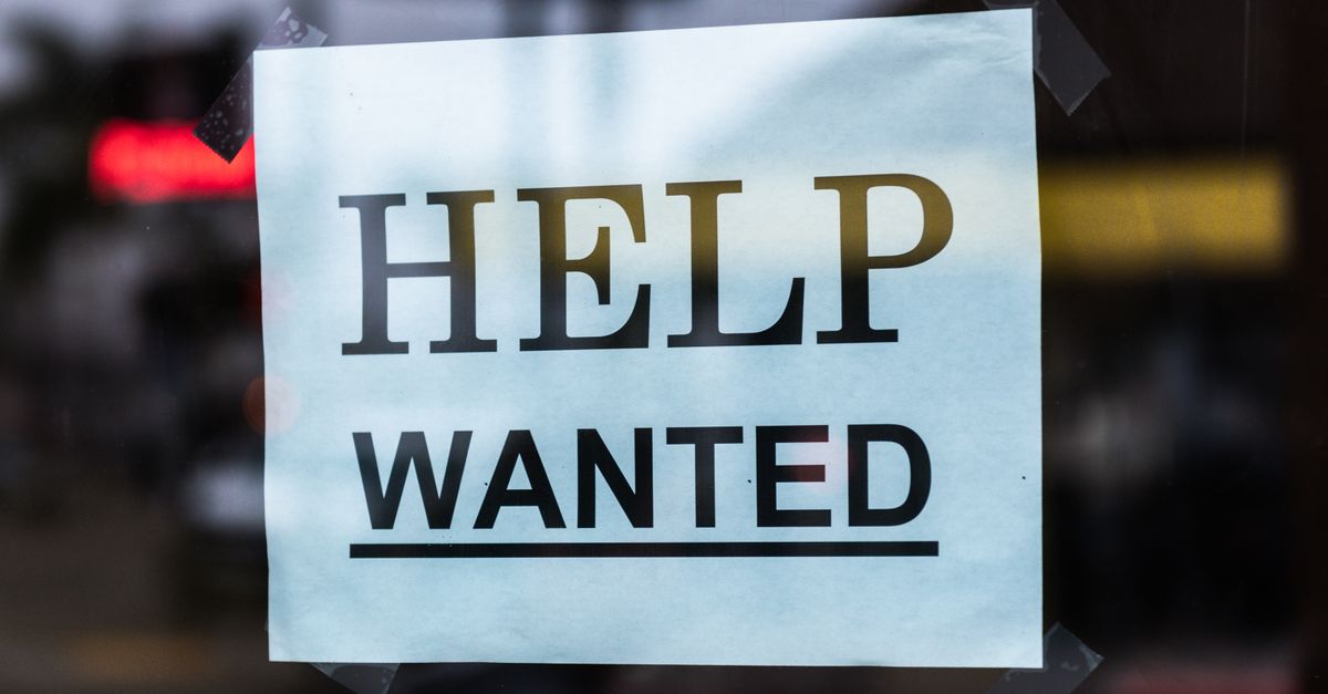 Close-up of a Help Wanted sign taped to a glass window in a storefront.